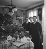 Tre kvinnor ståendes vid ett stort blomsterbord.