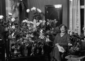 Porträtt. Kvinna sittandes vid blomsterbord.