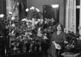 Porträtt. Kvinna sittandes vid blomsterbord.