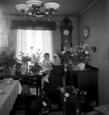 Kvinna med barn i knäet sittandes vid blomsterbord.