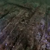 Tennlock som ligger löst på skrovpartiet. Hål i mitten. Fotad ovanifrån.