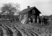 Familjena Larsson och Anderson framför stuga i Hovsta, 1920-tal