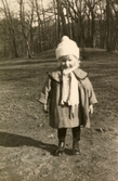 Lilla Karin Pamp (1923 - 1993) står på en gräsmatta, Stretered 1920-tal. Hon var dotter till en av personalen.
