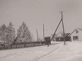 Fastarpsvägen i Tvååker. Foto från vintern 1941-1942. T h Bergendahls affär, t v därom en lagerbyggnad för diverse grövre varor oljor mm. T v mellan träden skymtar Gästgivaregården. Längts gatan står el- eller telefonstolpar.