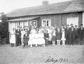 Gruppbild framför ett hus. Kvinnor, män och barn, stående och sittande.