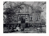 Mangårdsbyggnaden till Almebergs gård (Reisens) år 1900, kv Pilsberg i hörnet av Skansgatan - Ringvägen. Tre kvinnor sitter i trädgården nedanför verandan.