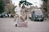 Poserande par med resväska framför lastbilar på Barnens dag, 1950-tal