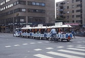 Turisttåg kör i sydvästra hörnet av korsningen Drottninggatan-Rudbecksgatan, 1987