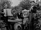 Spelmännen Sten Svensson och Erik Svensson med sällskap i en syrenberså. På bordet står en flaska och supglas. Under bordet står en trumma med cymbal. Sittande från vänster: Sten och Eriks far, Anders Svensson (han var stenhuggare och gjorde alla grunder till husen i Gällared under 1920-talet.), Bror Johansson, Roalyckan, Drängsered, Emil Johansson, Skogsgärde, Drängsered, Rut Svensson, Vismered, Artur Johansson, Bonnaberg, Gällared.