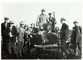 Ett jaktlag poserar med bössor och jakthund vid nedlagt byte. Älgen ligger på en kärra. Årnakulla, Krogsered 1932. Okänd fotograf.