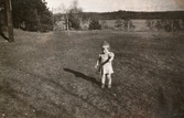 Lilla Eva Pettersson (gift Kempe) står på gräsmattan vid Stretereds personalbostad i Tulebo 1946. Mormor och morfar bodde där. I bakgrunden ses Tulebosjön.