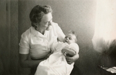 Karin Petterssons (gift Hansson) dopdag 1947-04-13. Modern Rosa Krantz (gift Pettersson) håller dottern i sin famn.
