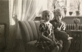 Systrarna Karin Pettersson (gift Hansson) och Eva (gift Kempe) sitter i soffan i föräldrahemmet på Gamlehagsvägen 17 i Torrekulla, år 1951. Eva håller första läxboken i handen då hon har börjat i 1:a klass.