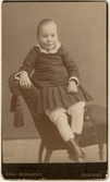 Flicka sittande på pall i fåtölj hos fotografen, ca 1887