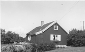 Bostadshus på Draget, Gottskär. Fönstren är försedda med fönsterluckor och till utbyggnaden finns en dörr. El- och telefonstolpar syns i bild.