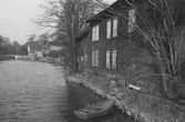 Bebyggelse vid Kungsbackaån med en eka förtöjd nedanför träbyggnaden i två våningar. En liten trappa vid båten leder upp till en tvåbladig port i fasaden. Till vänster ses Vallgatans bro över ån. (Se även bildnr G8520, G8521)