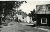 Bilden tagen midsommardagen 1944 av en gård belägen nedanför Vallda kyrka. Byggnaden närmast i bild har en utvändig trappa på gaveln till vinden.