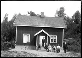 Grupporträtt, flera personer sitter framför ett hus. Palm.
Ur Gustaf Åhmans samling.