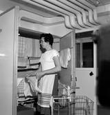 Kvinna hänger kläder i torkskåp i tvättstuga i Markbacken, 1960-tal