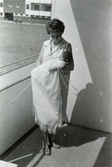 Ninnie Tobiasson (född Johansson, 1937) står på balkongen hållandes dottern Ilse (född 1960, gift Glimberg) i famnen, Bågskyttegatan 3g. Det är dotterns dopdag. Dopet skedde i Fässbergs kyrka av kyrkoadjunkt Sven Franzén den 17 april 1960.
