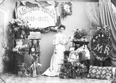 Mathilda Ranch firar 25-år som professionell fotograf den 25 maj 1907. Här poserar hon bland presenter och blomster i ateljén. Bland gåvorna märks en modell av ateljén i Varberg, en långsmal docka i smårutig kostym, textilier, en klocka i empirstil och en stor palett till höger med hennes initialer. Utöver olika buketter och blomsterarrangemang står krukor med hortensia respektive rhododendron till vänster.