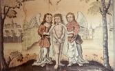 Detaljbild av väggmålning. Landskapsbild med stad i bakgrunden. I förgrunden två änglar, en på vardera sida om Jesus som har bundna händer.
Latinsk text med bland annat 