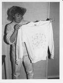 Tävling i Inside oktober 19 87, Gissa året. Elisabeth Sundström visar upp priser att vinna.
Hon håller upp en ljus collagetröja med tryck över bröstet.
Trycket består av bilar samt text BILAR nere th.
