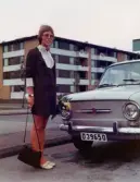 Karin Pettersson (gift Hansson), klädd i brudklänning och med en blombukett i handen, står brevid sin Fiat 650 utanför bostaden på Havrekornsgatan i Bifrost, 1973-09-29.