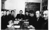 Nio män sitter samlade runt ett bord för studiecirkeln 
