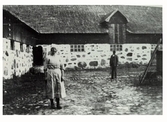 Mjölkerskan Hulda Severinsson vid ladugården på Lindhofs kungsgård. I bakgrunden står patron Walfrid Ljung. 1925.