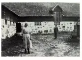 Mjölkerskan Hulda Severinsson vid ladugården på Lindhofs kungsgård. I bakgrunden står patron Walfrid Ljung. 1925.