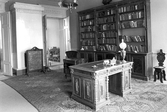 Kakelugn vid bokhyllor och skrivbord i biblioteket i Karlslunds herrgård, 1981