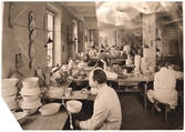 Målarsalen vid Gefle Porslinsfabrik där handmålade dekorer utfördes. Stående syns chefdekoratör Eugen Trost.
Foto från slutet av 1930-talet.