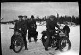 Gruppbild män i vinterkläder på isen vid Grunnerud. Två män på motorcyklar, en sittande på spark resten stående.