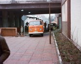 En orange folkabuss står parkerad under Mölndals Bro i Mölndals centrum, omkring 1975-1980. I bakgrunden bebyggelse på Broslätt.