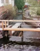 Vy från Forsebron mot industribebyggelse vid Mölndalsån i Mölndals Kvarnby, omkring 1975-1980. Till vänster gymnastiksalen.