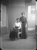 Ateljéfoto av två kvinnor, där en sitter på en taburett och den andra står bakom henne. Beställare och sannolikt avbildad: Klara Skog, Falkenberg.