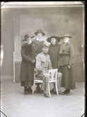 Ateljébild. Fyra unga kvinnor står kring en ung man i uniform med trekantig hatt, troligen är de syskon. Flickorna bär ytterkläder, ett par med pälsboa en med muff, och hattar. Beställare:  Sigrid Johansson. Se även bildnr GB2_1632)