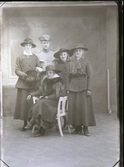 Ateljébild. Fyra unga kvinnor och en ung man i uniform med trekantig hatt, troligen är de syskon. Flickorna bär ytterkläder, ett par med pälsboa en med muff, och hattar. Beställare:  Sigrid Johansson. (Se även bildnr GB2_1631)