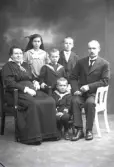 Ateljébild. Familjen Ringström, föräldrar med fyra barn. Makarna sitter med barnen stående mellan sig, utom den minste som sitter främst på en pall. Beställare: Ringström, Kemikalieaffären Falkenberg.