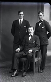 Ateljéfoto med tre herrar, varav en sitter. Beställare: Karl Holmgren, Gammelgården.