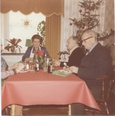 Tre personer sitter och äter julmat i Brattåshemmets matsal 1970-tal. I mitten ses Asta Ögren (biträde), till höger sitter en okänd man samt Per Pettersson (i glasögon).