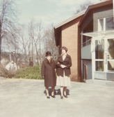 En kvinnlig boende samt en kvinnlig personal står utanför Brattåshemmets entré 1980-tal.