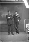 Ateljébild. Bilden föreställer två män stående i helfigur. Den ene bär sjömanskläder och den andre någon slags uniform med skepparkavaj och skärmmössa. Kanske är han beställaren N Johansson, med adress Morups fyr, och fyrvaktare eller dylikt. Fotograferat i Björkströms filial i Falkenberg.