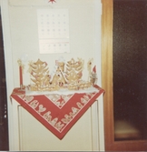 Ett juldekorerat mindre bord i Brattåshemmet 1970 - 80-tal. En del av dekorationerna är av pepparkaksdeg. På väggen ovanför bordet hänger en väggalmanacka.