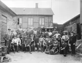 Arbetsstyrkan vid Varberg Mekaniska Verkstad omkring år 1900 samlad ute på gården. Med sig har männen olika verktyg som visar på deras profession; passare, tänger, klubbor, hammare, rubank med mera. Två män sitter dessutom på ett stort kugghjul. Här tillverkade man på beställning, främst redskap och maskiner som behövdes främst inom jordbruk och mejerinäringen men vissa produkter lagerhölls också. Förutom maskinavdelning fanns även snickeri- respektive plåtslageridel. Verkstaden startades på 1850-talet (då Ungewith & Co, spistillverkning) och drevs av olika personer fram till 1890-talet då Hugo Gerlach övertog företaget och brodern ingenjör Edmund Gerlach (död 1902) blev disponent. Verkstaden hade anlagts tämligen isolerat norr om den gamla trästaden, men vid det laget låg den mellan järnvägsstationen och den nya stenstaden, granne med de s k Tvillinghusen. Såsom ingenjörsdriven verksamhet fanns utöver gjuteri, maskinverkstad, smedja, magasin och koksbod även en ingenjörsbostad inom anläggningen. Enligt uppgift började arbetarna kl 6 och slutade 18.30. Maten fick de om vintern sitta och äta på ångpannan. (Se även bildnr VMA8141_1)

Sittande fr v: Skoog, Johan Svensson Bua, ?, Masen, Algot Svensson, Börje Ågren, Kastberg, Hillerström, Holmström, 