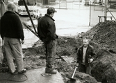 Under tiden nya Teaterhuset byggdes 1997 – 1998. Bilden är utomhus där en person grävt en stor grop som han står i. I handen håller han en spade. Bakom gropen som mannen står i är det en stor jordhög. Janne Sandberg, amatörteaterkonsulent, samt en okänd man står till vänster om gropen.