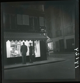 1950. Frankrike. Kvällsbild, två män framför skyltfönster