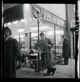 1950. Paris. Man står och läser tidning vid en bar