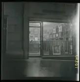 1950. Paris. En man sittter inne i en butik med konst, kväll